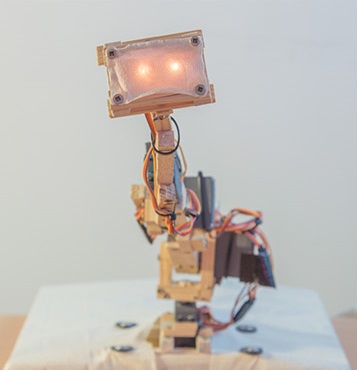 Adelino, the craft robot — a wooden robot with a glowing LED eye panel and exposed servos and wiring