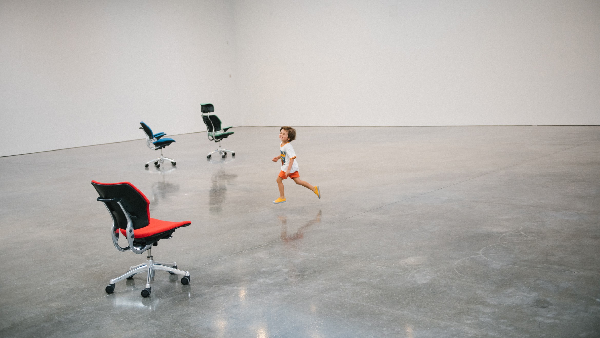 A child running past robotic office chairs in the white gallery space of PLAY at the Gagosian Gallery, New York